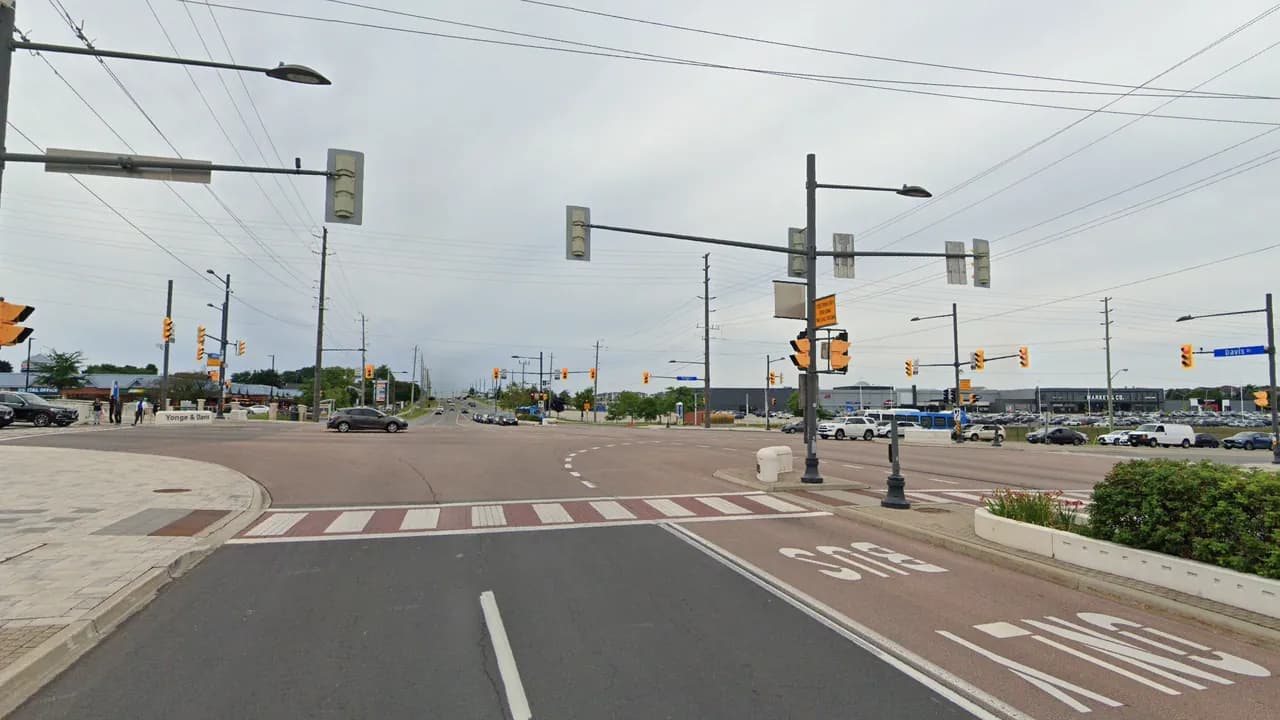Davis Drive at Yonge Street in Newmarket, looking west across the intersection past a red bus-only lane, with plazas on the far corners