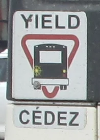 YIELD sign with a bus inside a red triangle, above a CÉDEZ panel, on the back of a transit bus
